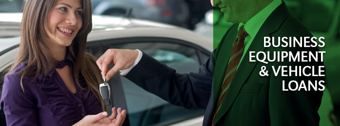 A smiling woman in a purple blouse accepts the key to a new car from a business auto dealer.