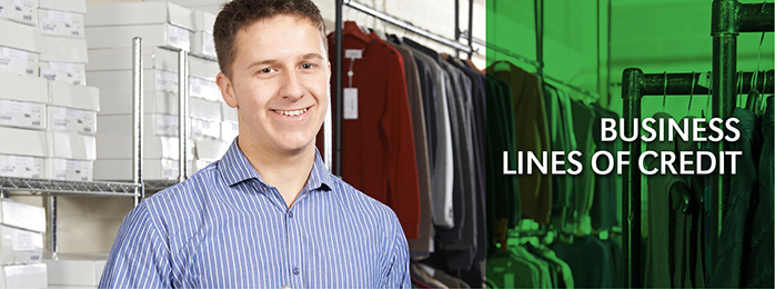 A happy business man in a striped collared shirt stands in front of inventory at his clothing store.