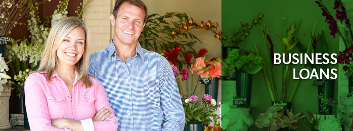 A smiling man and woman in business together welcome you to their flower shop.