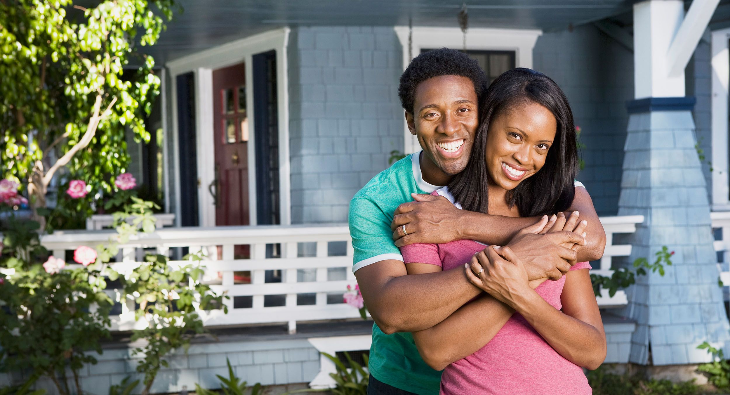 A young married couple embrace in front of their newly purchased home.